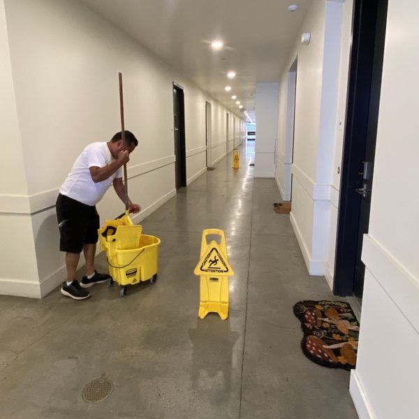 Oscar mopping a hallway with a bucket and a wet-floor sign